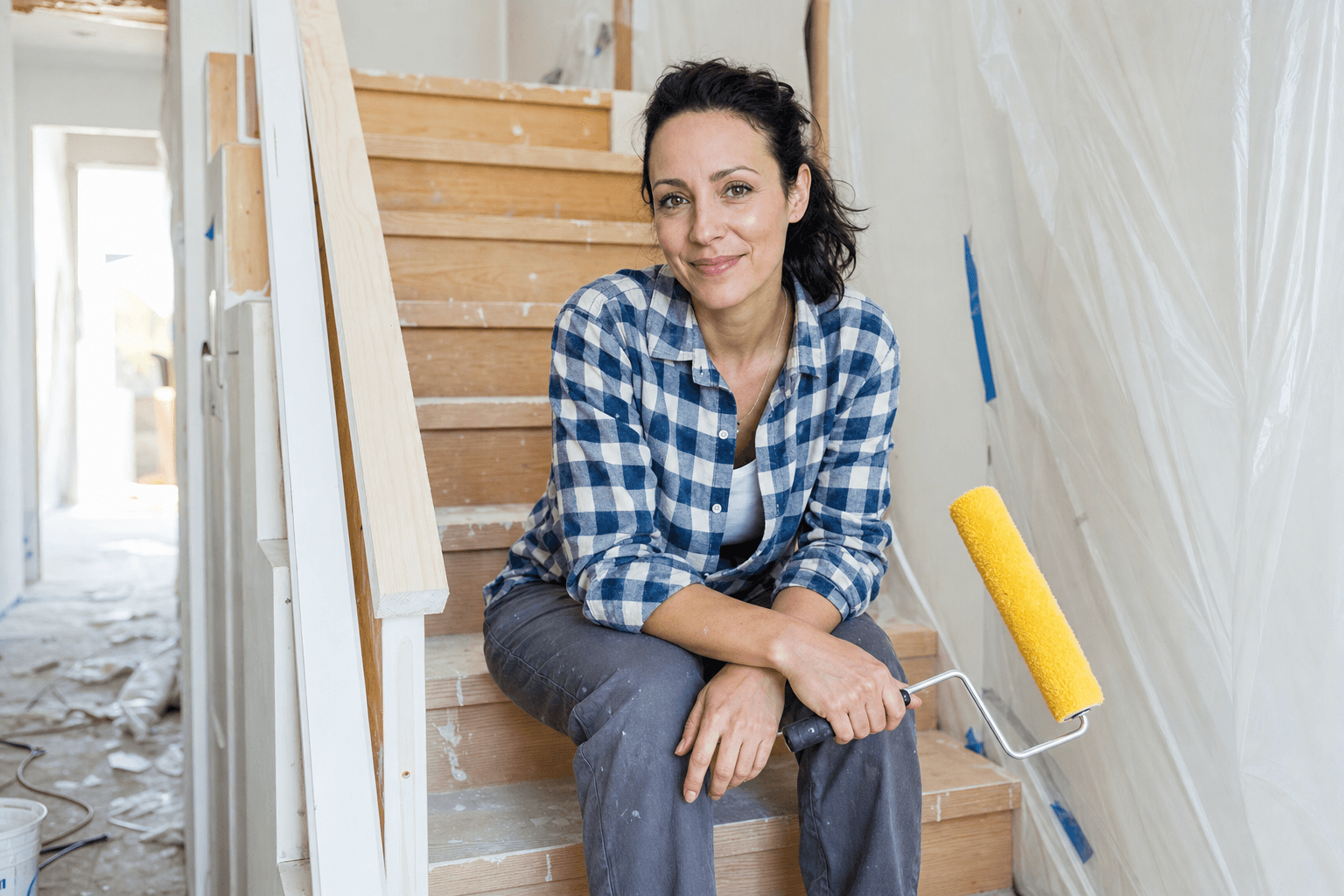 Homeowner sitting on wooden stairs with a paint roller during a home renovation